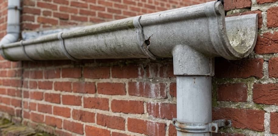 Grijze asbestcement dakgoot en regenwaterafvoerbuis langs gevel van oudere Belgische woning